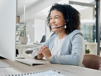 Eine Frau sitzt lächelnd im Büro und ist am telefonieren