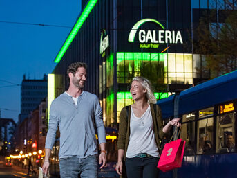 Paar auf Shoppingtour am Abend, im Hintergrund die Kasseler Galeria-Filiale