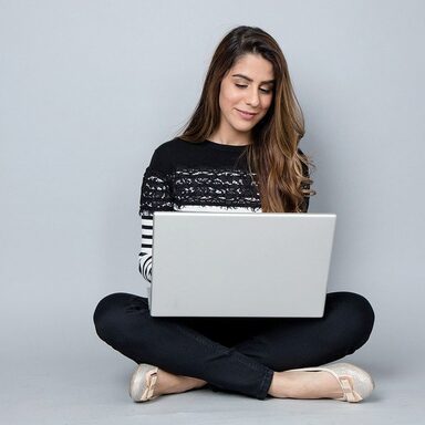 Eine Frau sitzt im Schneidersitz und hat einen Laptop auf ihrem Schoß.