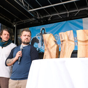 Drei Holzskulpturen auf einem Tisch recht im Bild, daneben stehen die Gestalter des Werkhofs am Parkschönfeld und schauen auf die Skulpturen