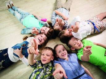 Group of happy kids laying in star shape on the floor with lifted hands