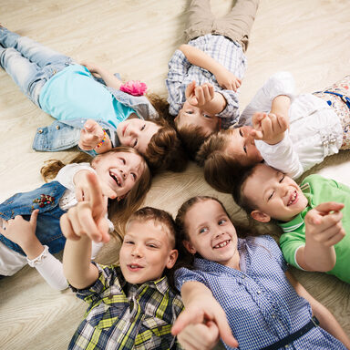 Group of happy kids laying in star shape on the floor with lifted hands
