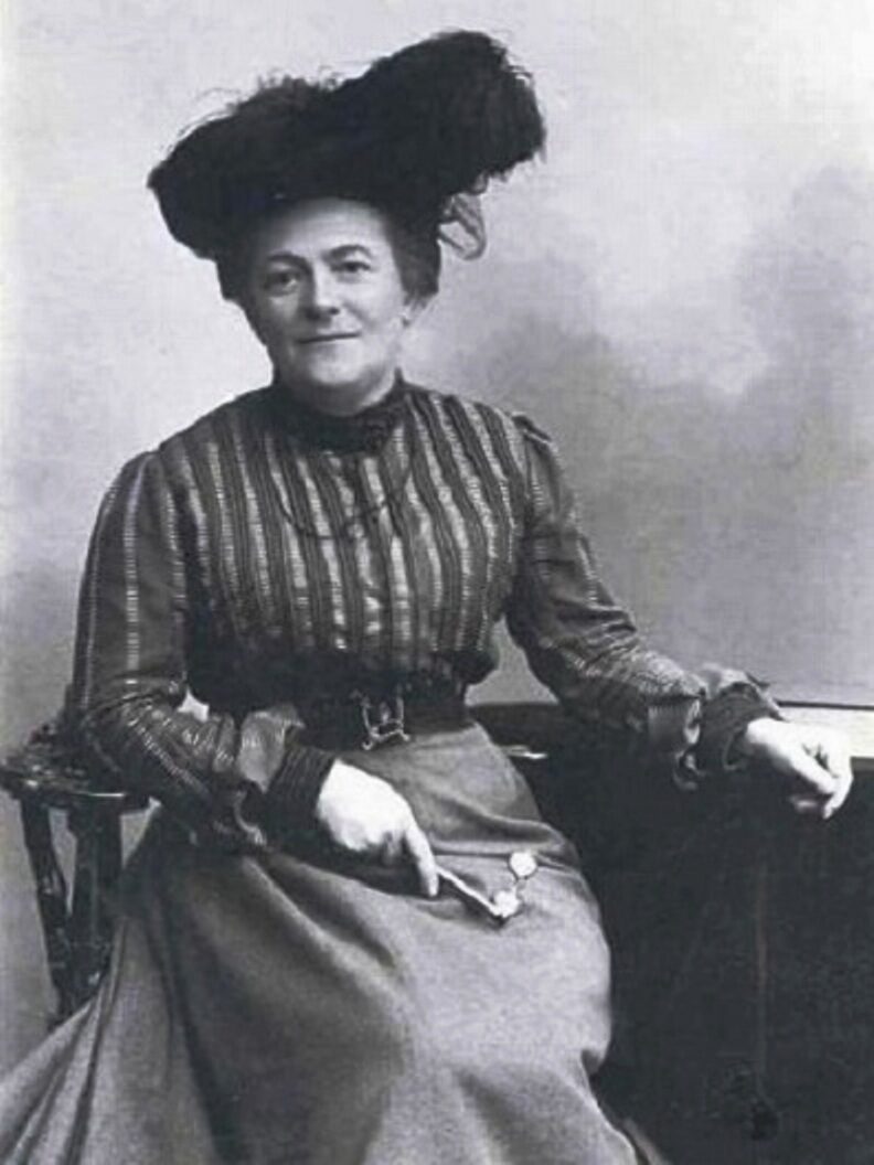 Clara Zetkin, sitzend in zeitgenössischer Kleidung mit Hut