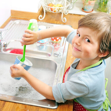 Ein Junge wäscht eine Tasse am Spülbecken ab