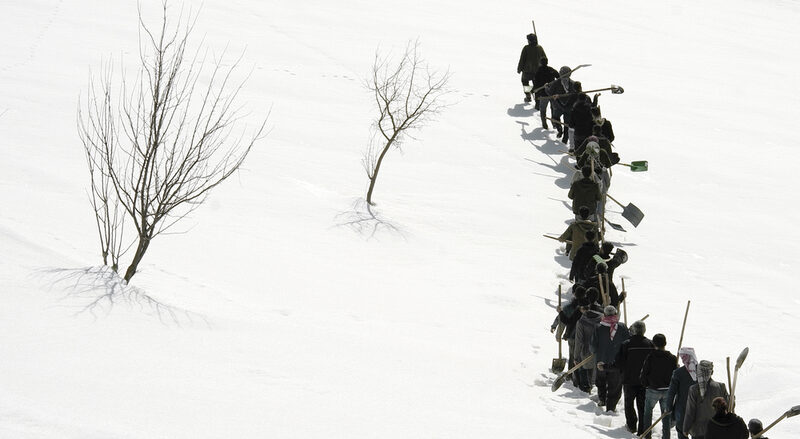 Schwarz Weiß Bild mit einer Reihe von Arbeitern in einer verschneiten Landschaft. Dazu mehrere kahle Bäume