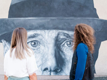 Zwei Personen vor einem Wandbild von Joseph Beuys