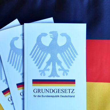 Drei Ausgaben des Grundgesetzes vor Schwarz-Rot-Gold, den darin festgelegten Farben der Bundesrepublik Deutschland