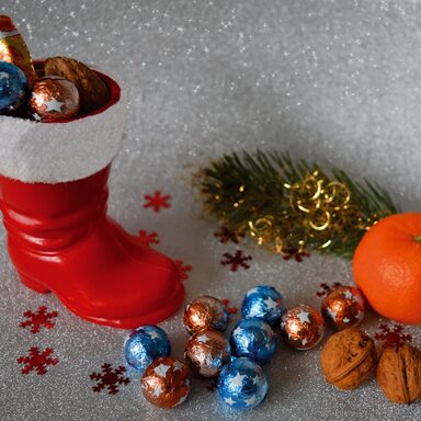 Roter Weihnachtsstiefel mit Schokoladenkugeln, Sternen, Nüssen sowie Mandarine, Tannenzweig
