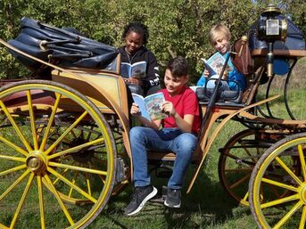 Drei Kinder sitzen in einer Kutsche und lesen