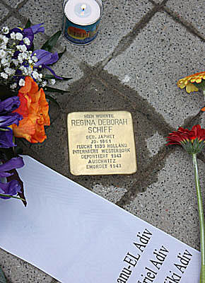 Stolperstein für Regina Deborah Schiff, gesäumt von Blumen, Trauerschleife mit Namen der Nachfahren und Kerze