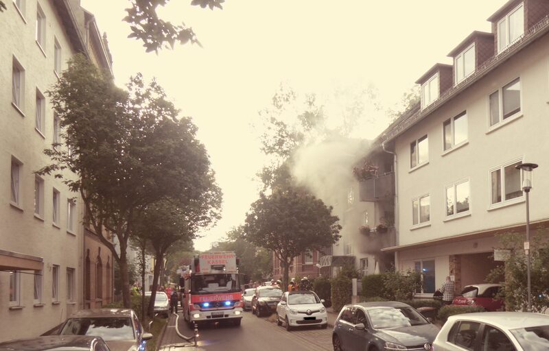 Aufnahme von der Straße mit Löschzug und einer Rauchwolke, die aus einem Gebäude austritt.