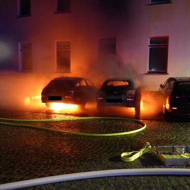 Brennende Fahrzeuge vor Gebäude