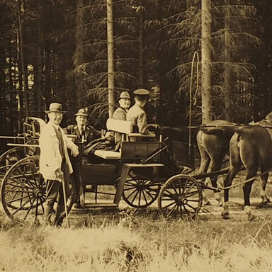 Vergilbtes Schwarz-Weiß-Foto von vier Personen in bzw. vor einer Pferdekutsche im Wald.