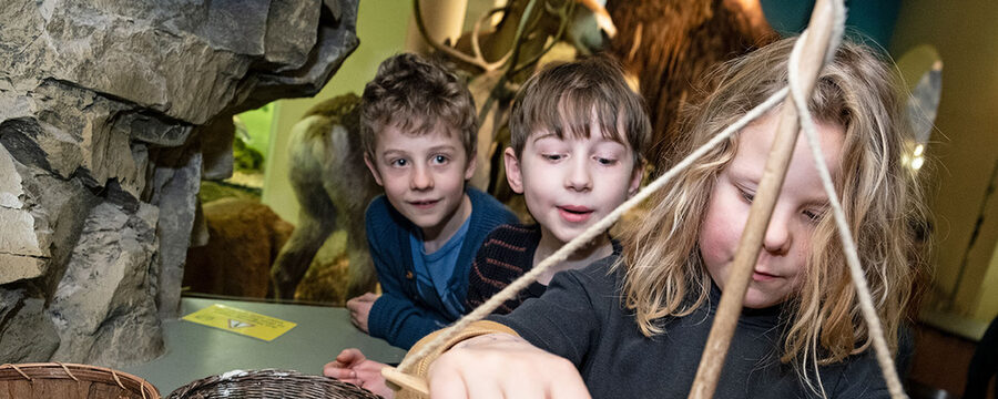 Kinder bohren mit einem Steinzeitbohrer aus Holz auf einer Scheibe.