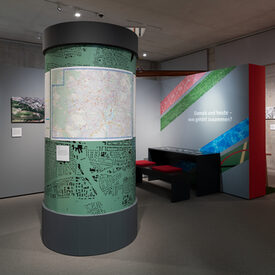 Blick in die Sonderausstellung „Es lebe der Sport!“ mit Sicht auf eine Litfaßsäule, an der eine Karte von Kassel hängt.