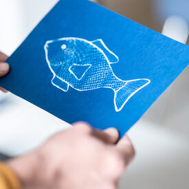 Jemand hält einen blauen Fisch, der mit Cyanotypie erstellt wurde.