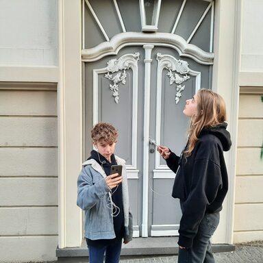 Zwei Jugendliche hören den Audiowalk vor einem historischen Gebäude