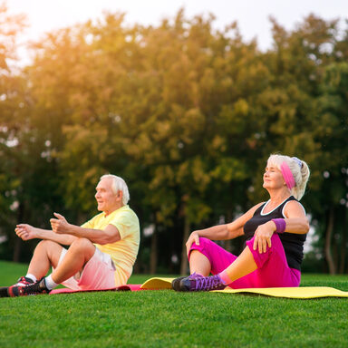 Senioren sitzen im Sommer auf einer Wiese und machen Yoga