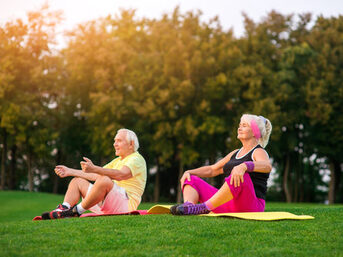 Senioren sitzen im Sommer auf einer Wiese und machen Yoga