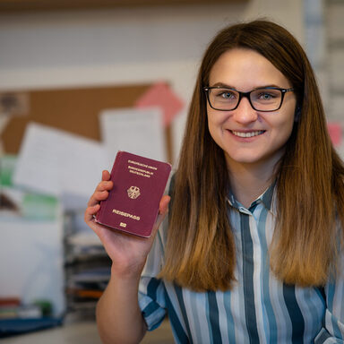 Eine junge Frau mit Brille zeigt stolz ihren Reisepass