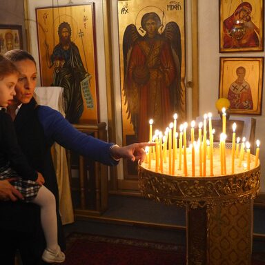 Frau mit einem Kind auf dem Arm vor einer Schale mit Kerzen
