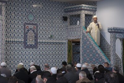 Iman der sunnitischen Moscheegemeinde mit knienden Männern im Vordergrund