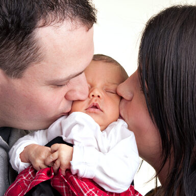 Ein neugeborenes Baby wird von ihrem Vater und Mutter auf die Wange geküsst
